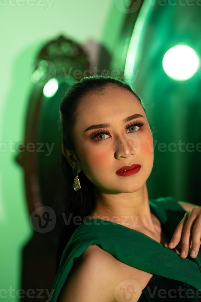 un artista mujer con un verde vestir y bufanda posando muy hermosa y exótico en frente de un maquillaje espejo en un verde habitación foto