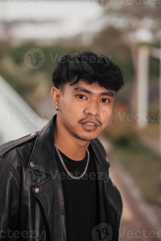 un asiático hombre con un travieso cara vistiendo un cadena collar y un negro cuero chaqueta en un café foto