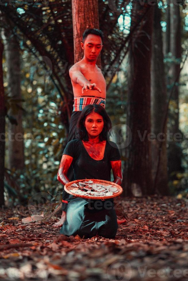 an Asian woman and man were standing in front of a tree while hunting an animal in the middle of the forest until they were covered in blood photo