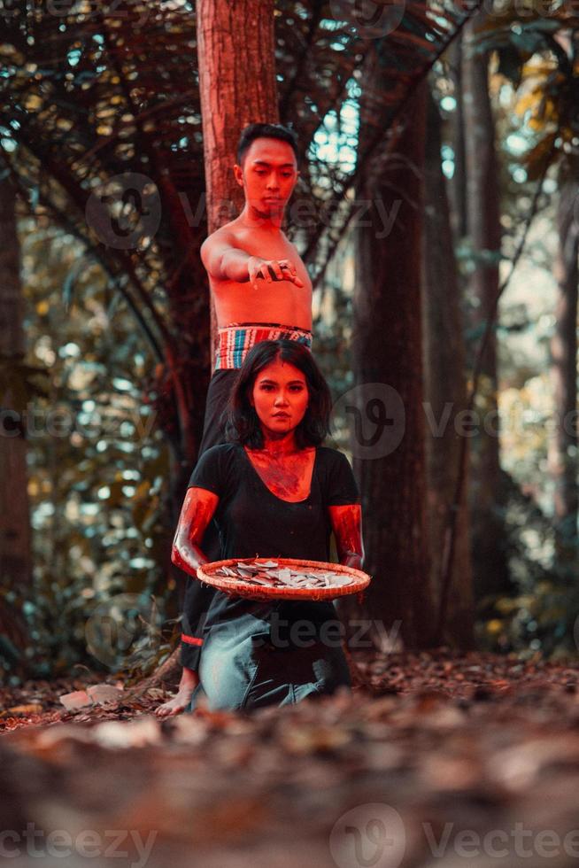an Asian woman and man were standing in front of a tree while hunting an animal in the middle of the forest until they were covered in blood photo
