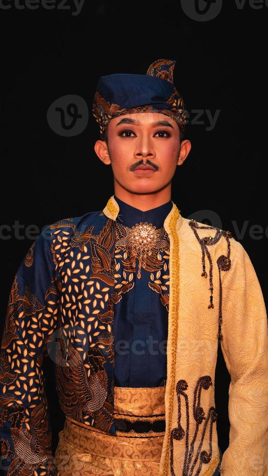 an Asian man wearing a traditional Indonesian dance costume is brown and his face is full of makeup photo