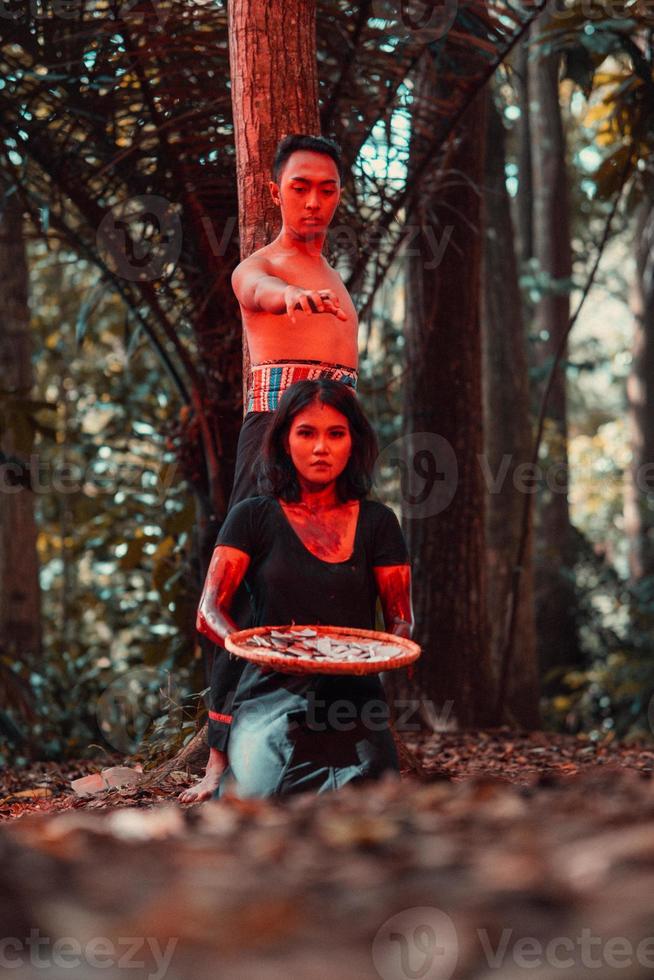 an Asian woman and man were standing in front of a tree while hunting an animal in the middle of the forest until they were covered in blood photo