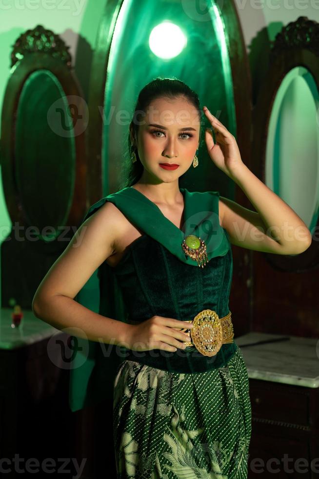 un artista mujer con un verde vestir y bufanda posando muy hermosa y exótico en frente de un maquillaje espejo en un verde habitación foto