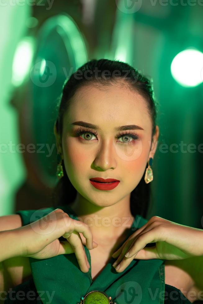 a beautiful Asian woman in a green dress is posing with her hands very gracefully and has green eyes photo