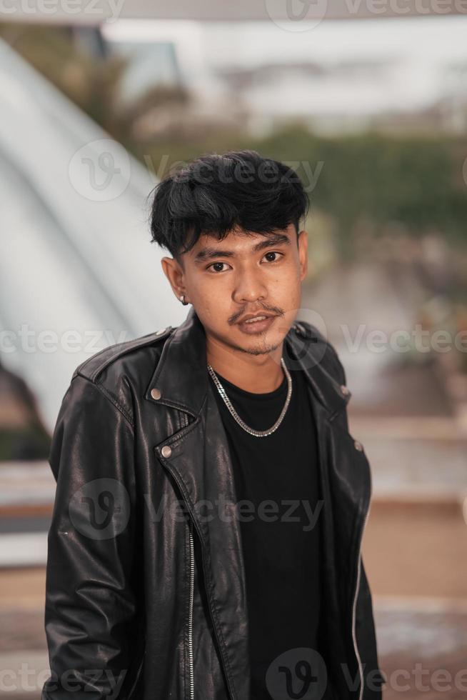 an Asian man with a naughty face wearing a chain necklace and a black leather jacket in a cafe photo