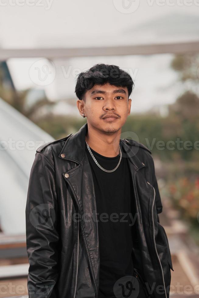 un crecido hombre en un negro cuero traje y cadena collar posando muy gallardamente en el ancho foto