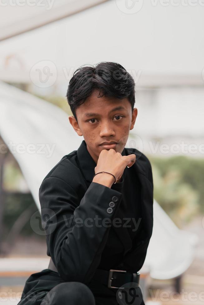 an Asian teenager in a black denim jacket leans against a garden table while relaxing and enjoying the view photo