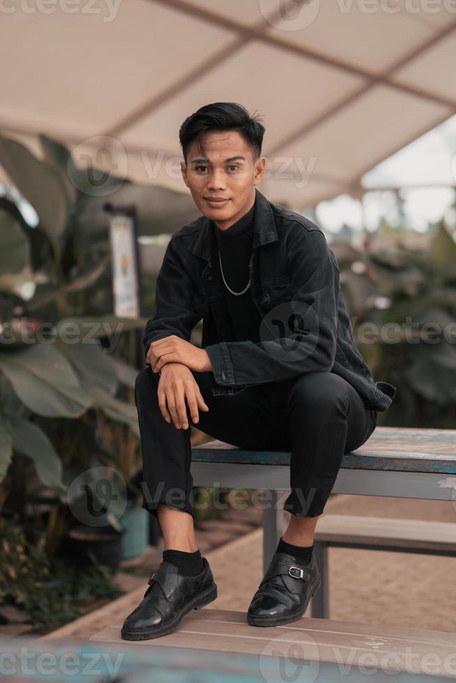 an asian boy in a black denim jacket posing like a naughty boy with a chain around his neck in a park photo