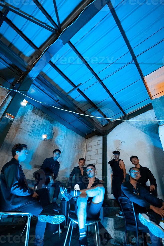 a group of Asian teenagers in black clothes sitting together in a black building with a blue light on the room photo