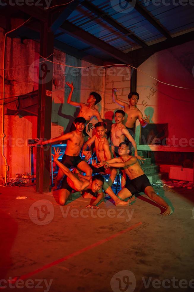 a group of men without clothes dancing poses in an old building with a red light photo