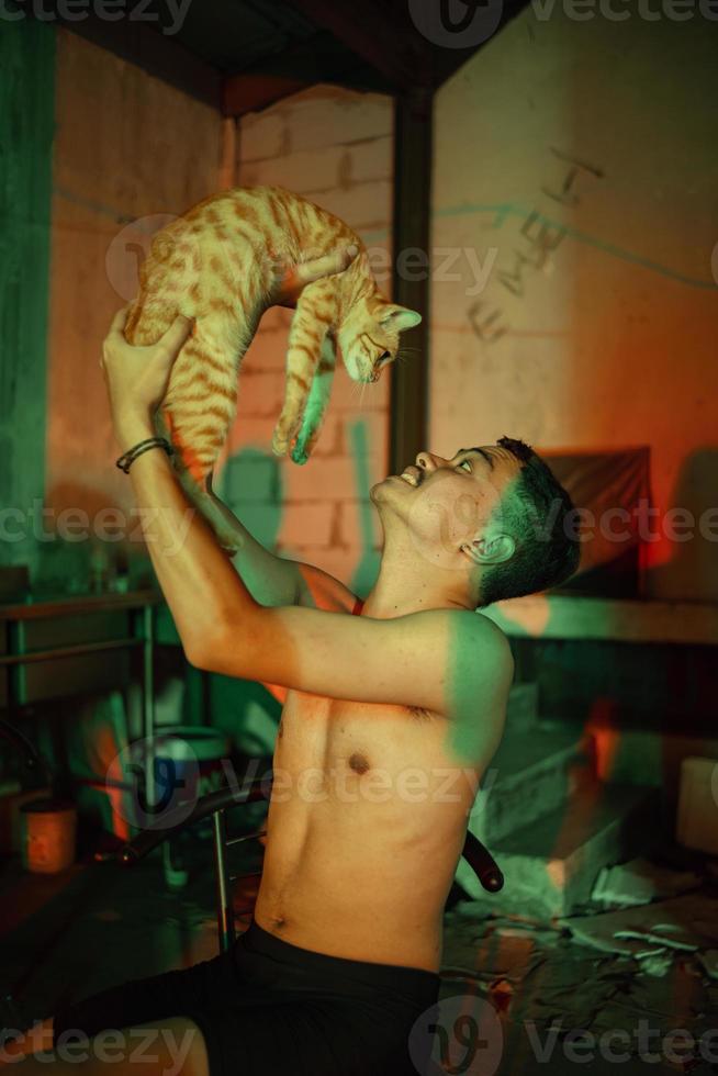 a man in black shorts holding an orange cat in a building with colorful lights photo