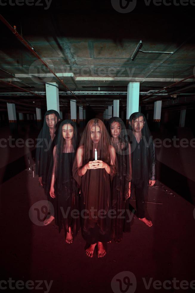 a group of devil worshipers in all black clothes and transparent veils holding candles together during a worship ritual in a building photo