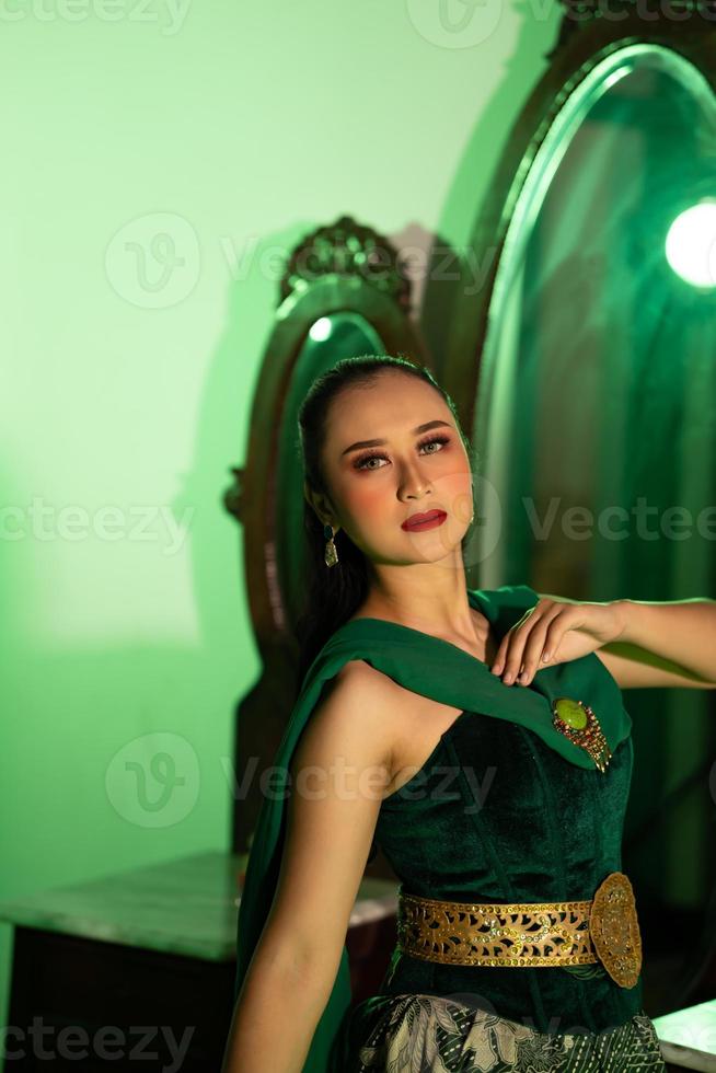 a entertainer woman with a green dress and scarf posing very beautiful and exotic in front of a makeup mirror in a green room photo