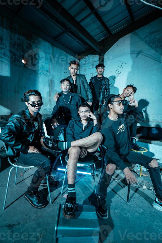 a group of Asian teenagers in black clothes posing very coolly while sitting in a warehouse chair which is lit blue photo