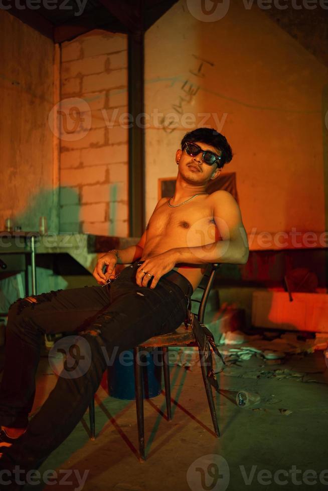 un gay chico en Gafas de sol y mezclilla pantalones posando muy travieso foto