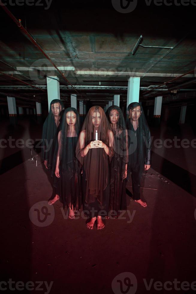 a group of devil worshipers in all black clothes and transparent veils holding candles together during a worship ritual in a building photo