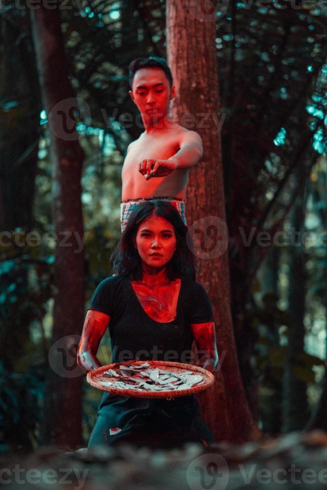 an Asian woman and man were standing in front of a tree while hunting an animal in the middle of the forest until they were covered in blood photo