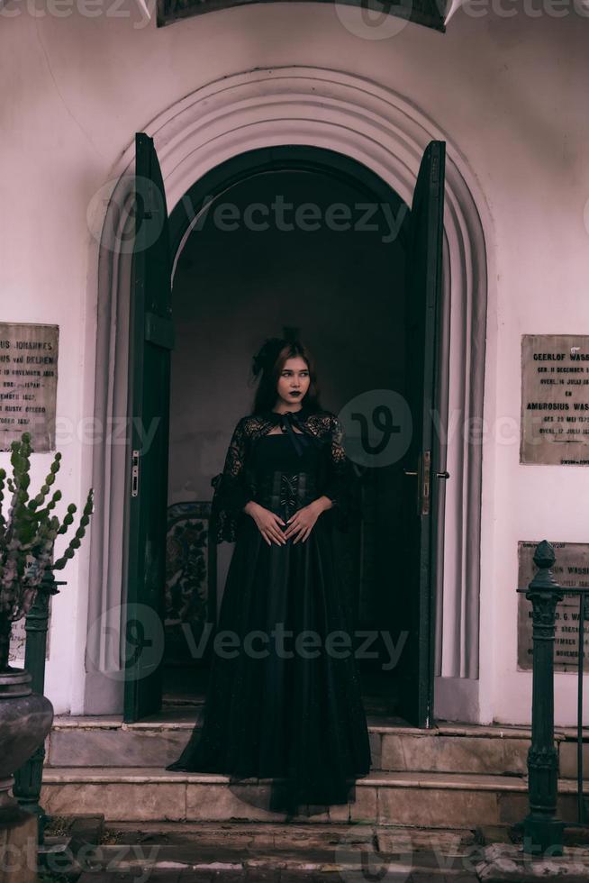 an Asian woman with lips and a black dress standing in front of an open door while visiting a cemetery photo