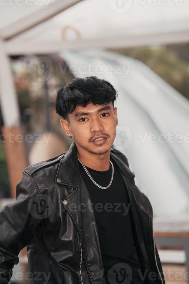 a grown man in a black leather suit and chain necklace posing very dashingly in the broad photo