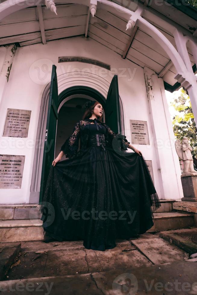 a witch in an all black dress walks down the steps of a cemetery after visiting her deceased brother photo