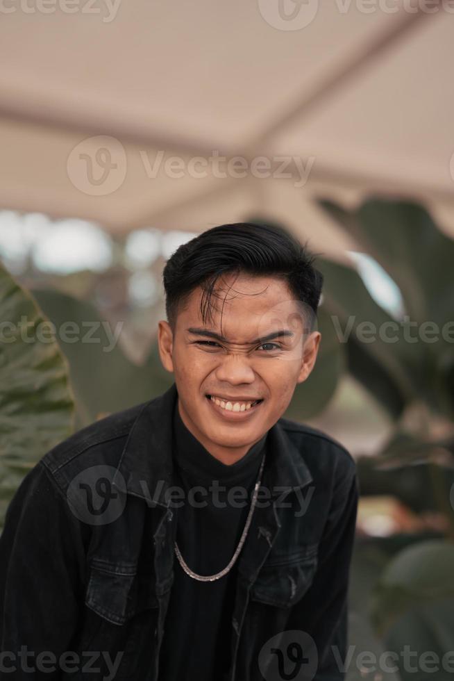 un asiático hombre en un negro mezclilla chaqueta posando con un alegre cara y muy hermoso en un café foto