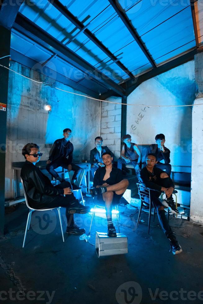 a group of Asian teenagers in black clothes sitting together in a black building with a blue light on the room photo