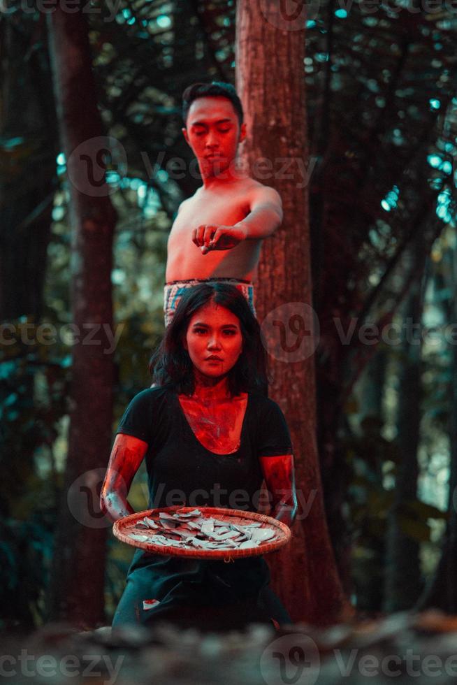 an Asian woman and man were standing in front of a tree while hunting an animal in the middle of the forest until they were covered in blood photo