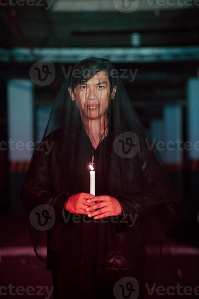 un masculino diablo adorador con un transparente velo es ejecutando un escalofriante ritual por participación un vela en su mano foto