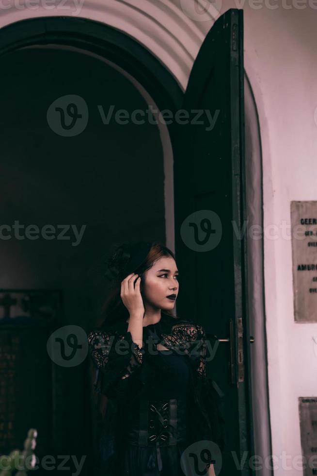 an Asian woman with lips and a black dress standing in front of an open door while visiting a cemetery photo