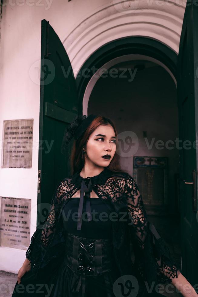a witch in an all black dress and scary makeup was standing at the cemetery gate photo