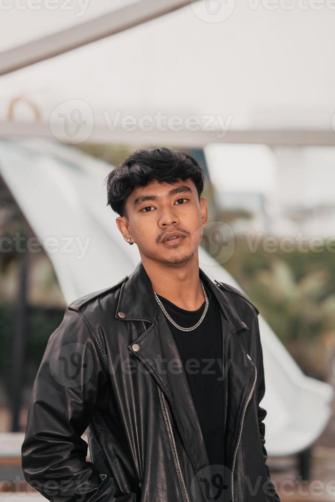 a grown man in a black leather suit and chain necklace posing very dashingly in the broad photo