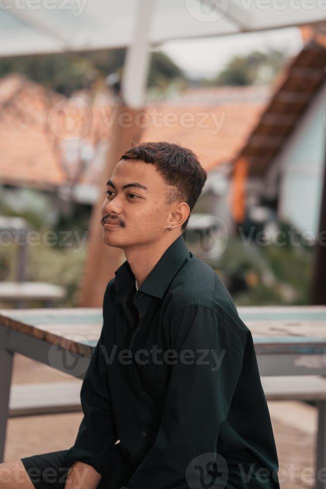 an Asian man with a handsome face and mustache wearing a black shirt while relaxing photo