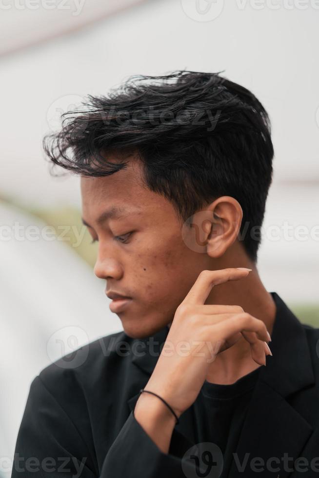an Asian teenager in a black denim jacket leans against a garden table while relaxing and enjoying the view photo