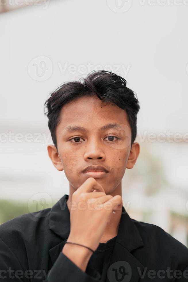 an Asian teenager in a black denim jacket leans against a garden table while relaxing and enjoying the view photo