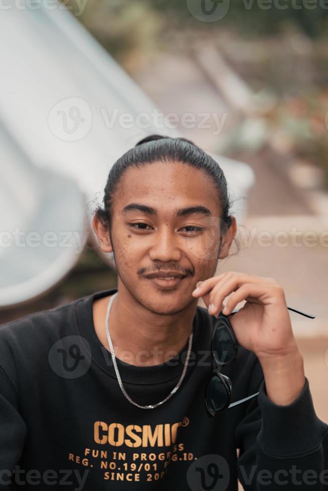 an Asian man with his hair tied up and wearing a black sweater jacket is sitting relaxing at a cafe table when meeting his friends photo