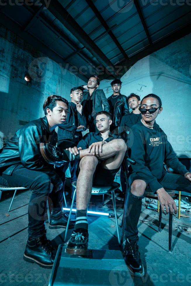 a group of Asian teenagers in black clothes posing very coolly while sitting in a warehouse chair which is lit blue photo