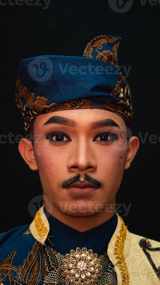 an Asian man wearing a traditional Indonesian dance costume is brown and his face is full of makeup photo