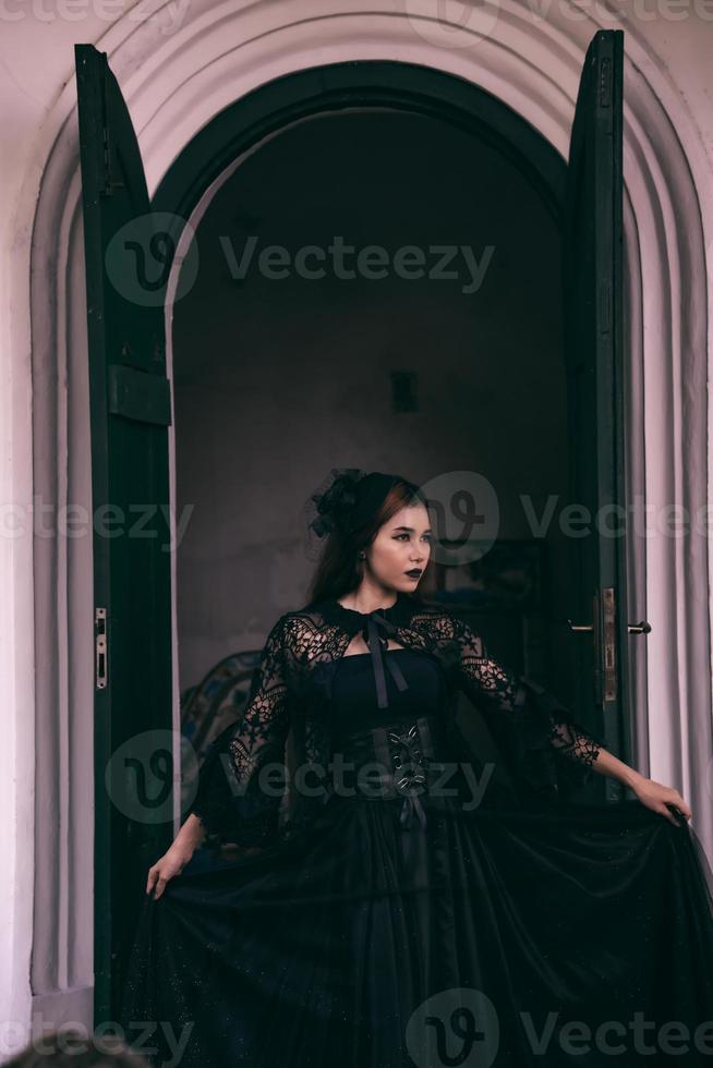 an Asian woman with lips and a black dress standing in front of an open door while visiting a cemetery photo