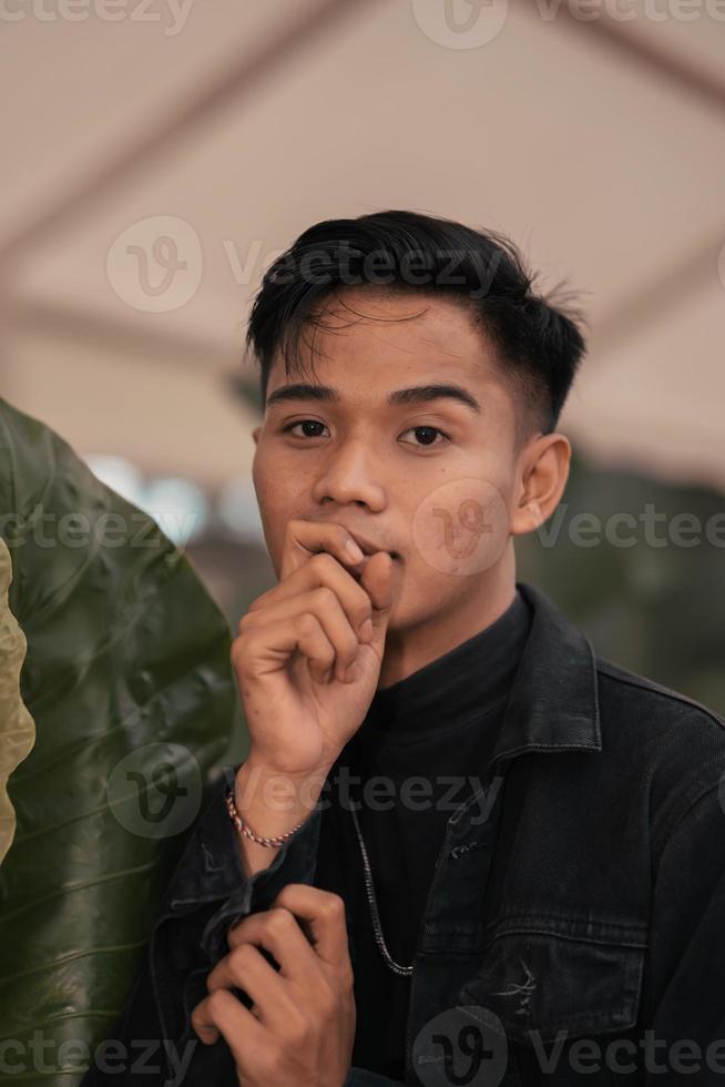 an Asian man in a black denim jacket posing with a cheerful face and very handsome in a cafe photo