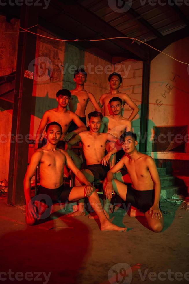 a group of men without clothes dancing poses in an old building with a red light photo