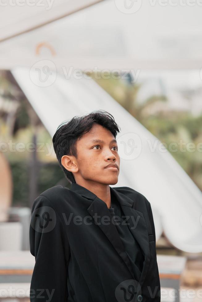 an Asian teenager in a black denim jacket leans against a garden table while relaxing and enjoying the view photo