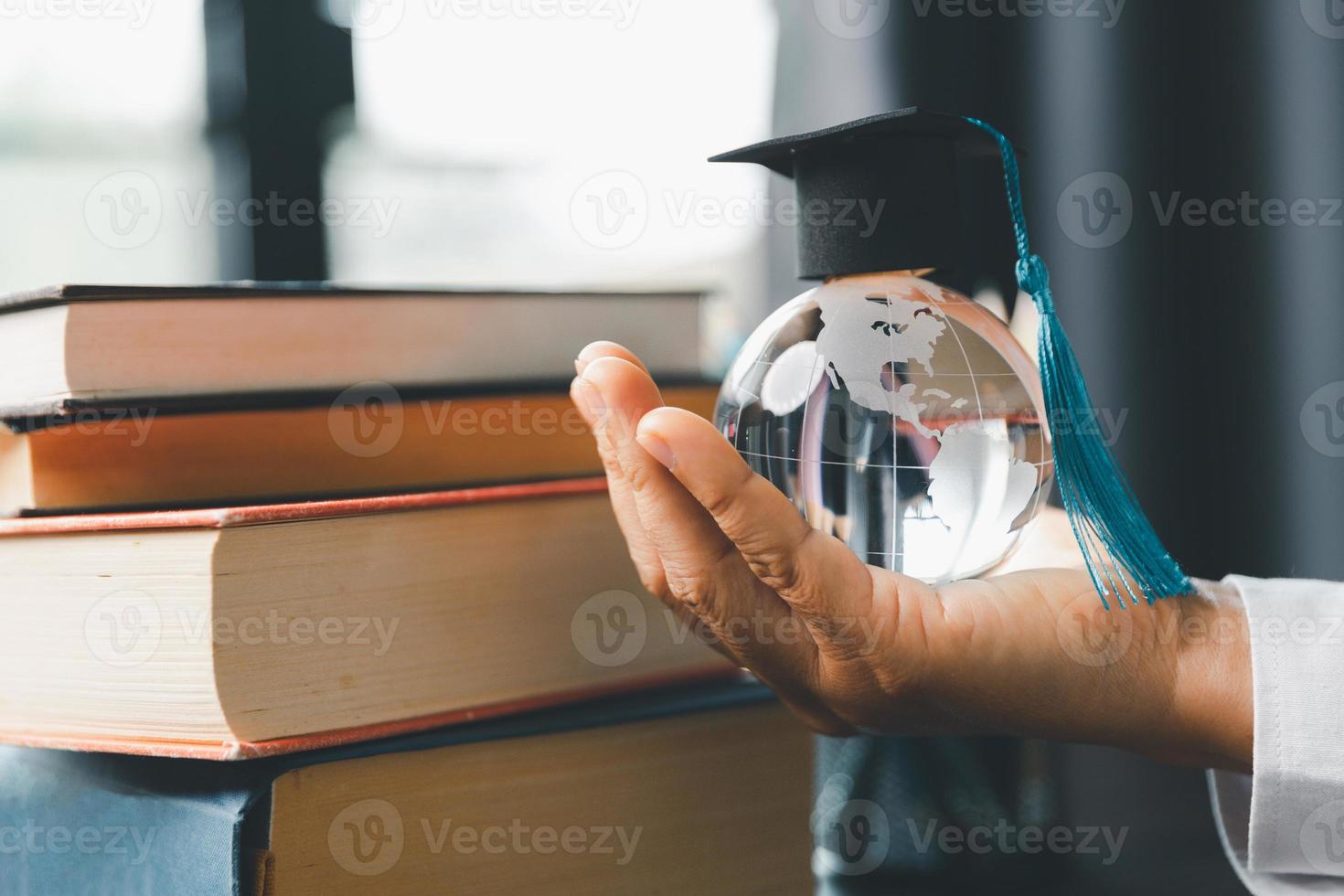 Graduate study abroad program concept  Black graduation cap on a globe map and books, depicts knowledge can be learned online anywhere and everywhere, even in universities or campus around the world. photo