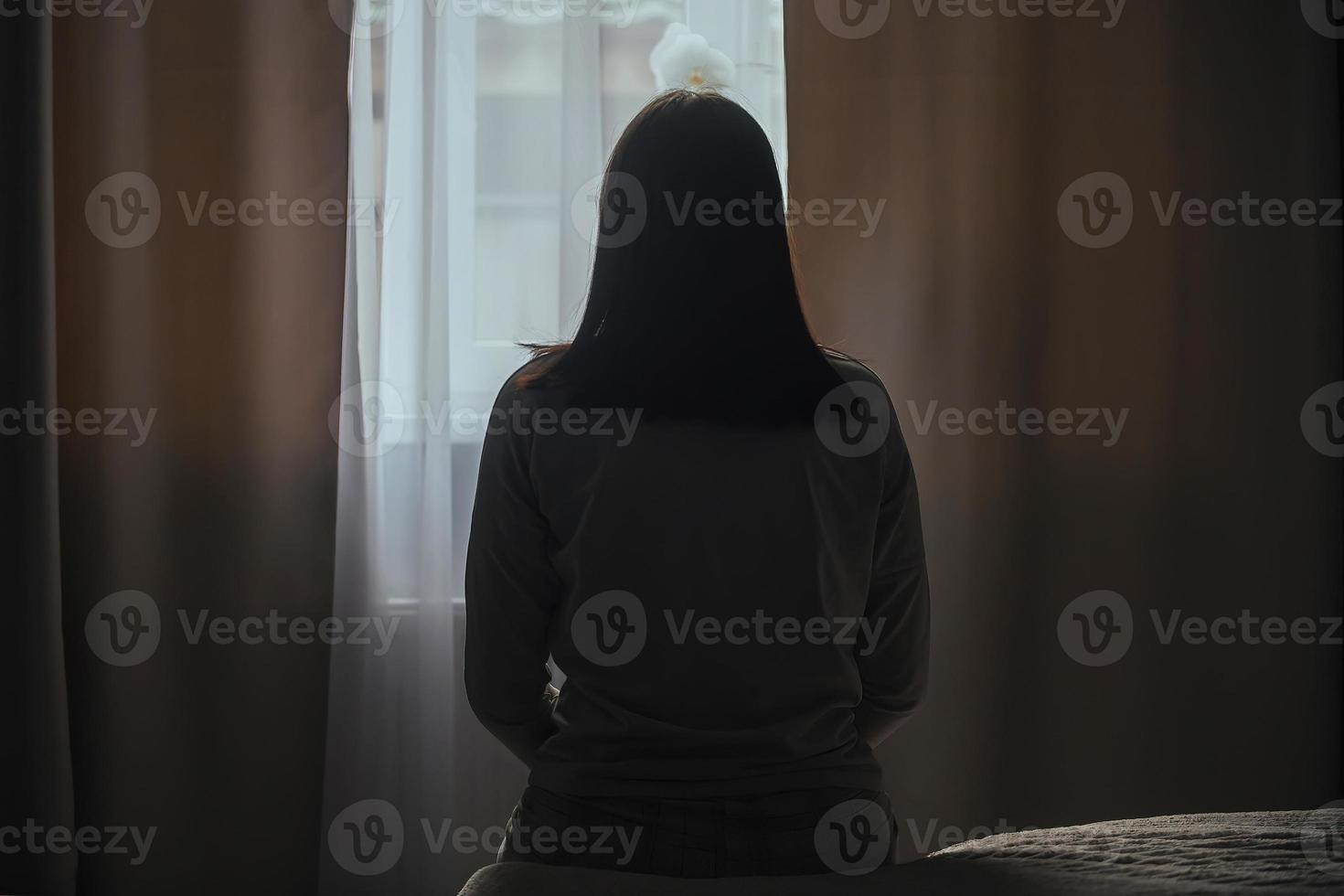 Silhouette of a young woman in pajamas against the background of a window at home on a bed with seasonal affective disorder or depression. The concept of winter depression due to lack of sunlight photo