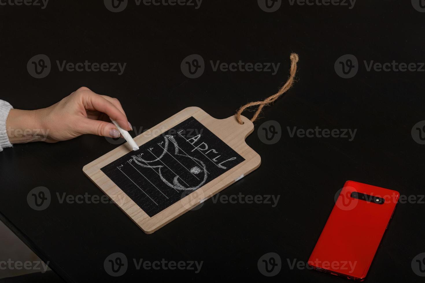 Conceptual image of the calendar day April 1 with empty space for text on a dark background in the form of a note on a board and a picture of a fish, next to the phone. April Fool's Day photo