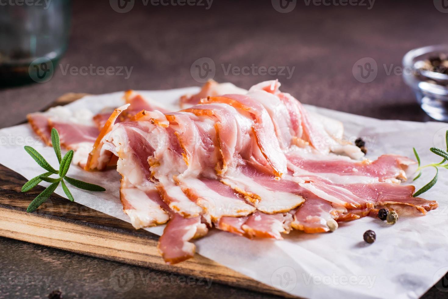 Raw smoked bacon and rosemary on a cutting board on the table. Hearty snack. photo