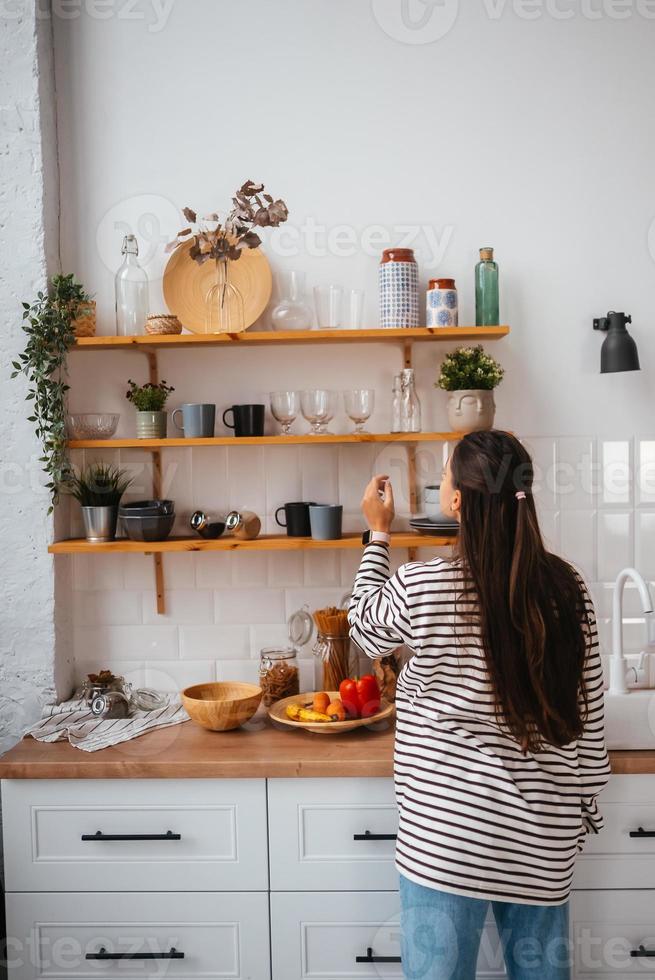 Woman takes out a glass from shelf in the kitchen photo