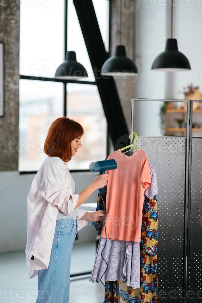 Beautiful young housewife irons clothes with a steamer at home. photo