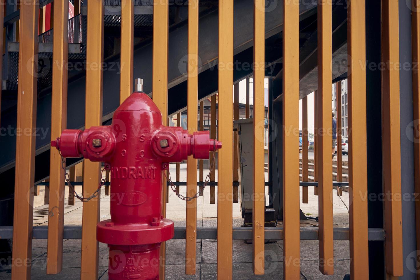 Close up of a red fire hydrant with two arms on both sides. Golden fence background. Stand Pipe Hydrant outdoor with copy space. photo