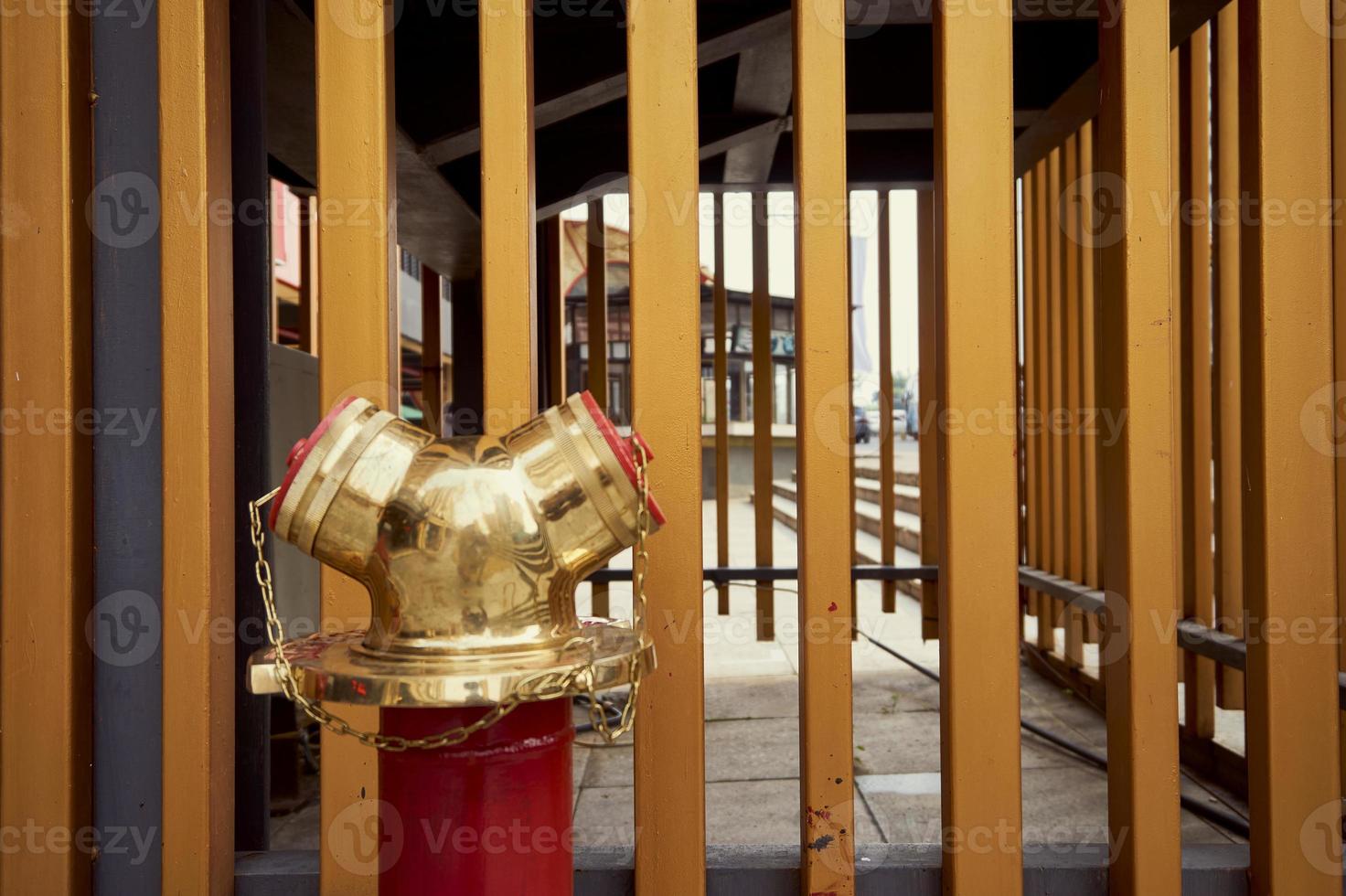 A Siamese Connection or splitter in fire protection system with standpipe riser for supply water when fire accident or emergency. Fire fighting. Fire department connection with golden fence background photo