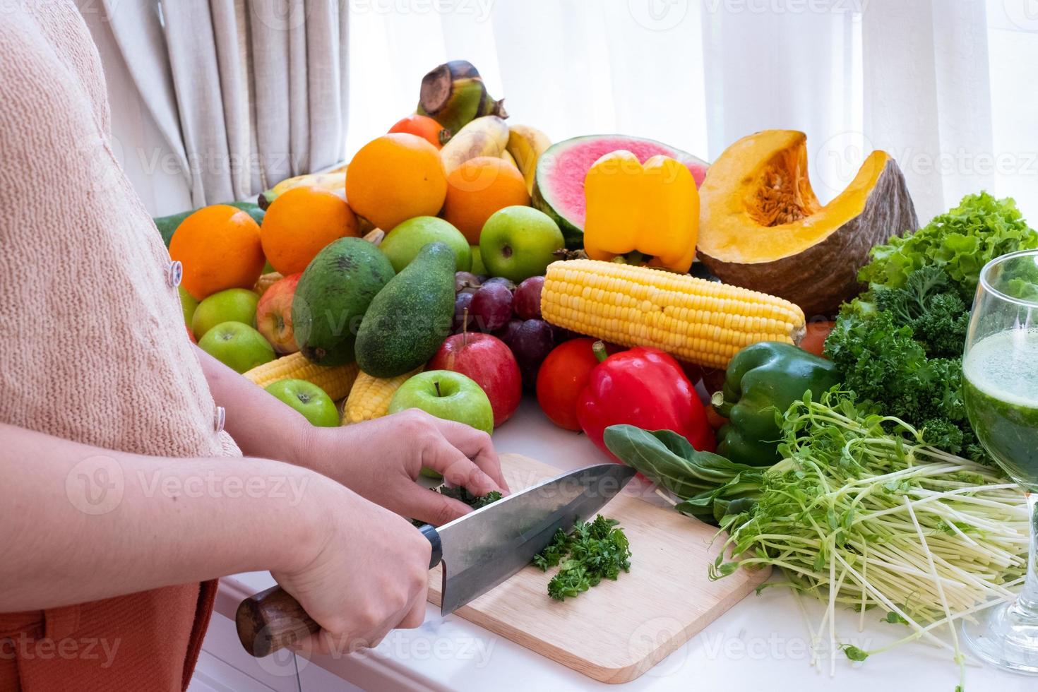 a person's hands are visible holding a knife and chopping vegetables on a cutting board with fruit the background is a white curtain photo